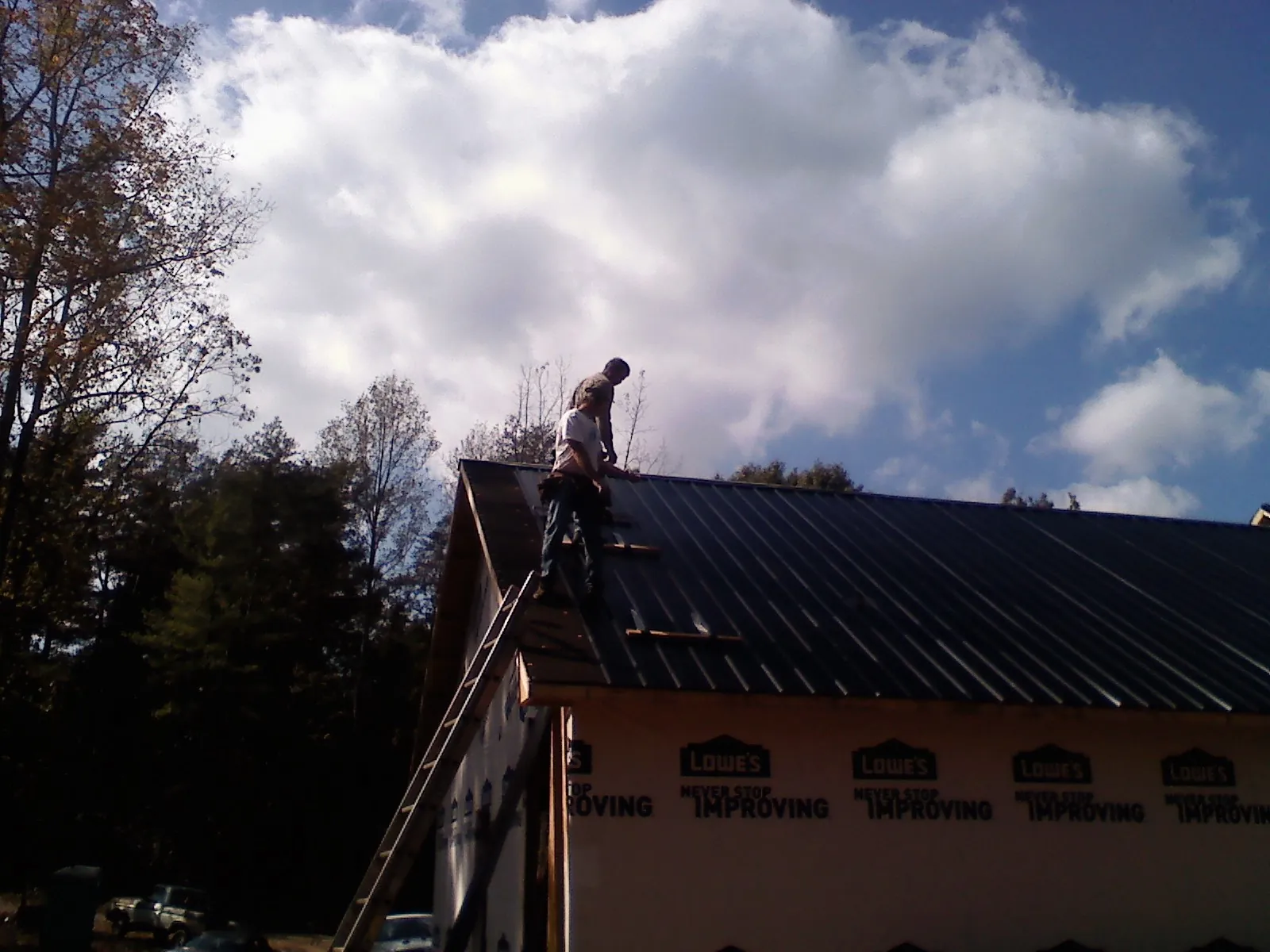 Roofer fastening dark metal panels high against a cloudy sky, from a Roof Inspection job in Hot Springs